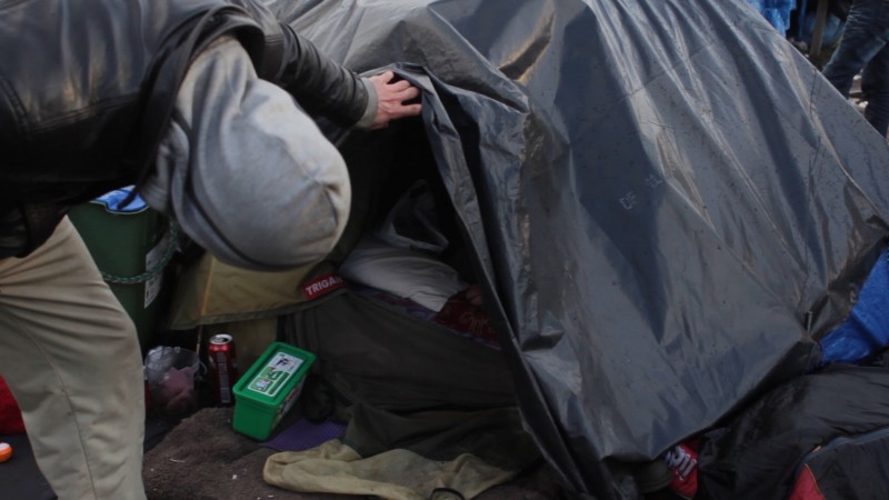 Seen from behind, a man leans down to look into his small, cluttered tent in the refugee camp in Calais, France. The faces of the documentary's subjects are hidden, because all feared for their safety as refugees from the violence in Syria. (Amel Guettatfi)