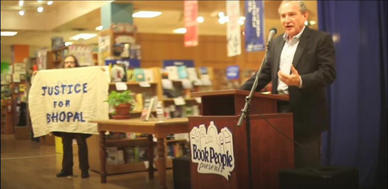 Kit O'Connell confronts George Friedman, CEO of Strategic Forecasting (Stratfor), at a book signing while holding a banner reading Justice For Bhopal. Multiple activists disrupted this event at Book People in Austin, Texas. Emails obtained by WikiLeaks from Anonymous revealed that Dow Chemical paid Stratfor to spy on nonviolent activists seeking justice for the Bhopal, India chemical disaster. (Screenshot)