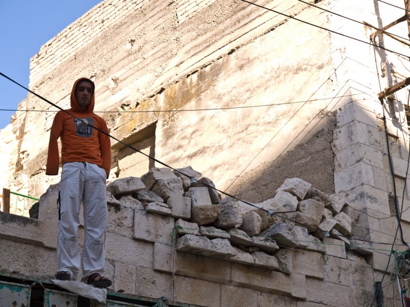 File: A Palestinian teenager stands on part of the facade of a damaged stone building in Hebron, May 9, 2008. (Flickr / Apaché)