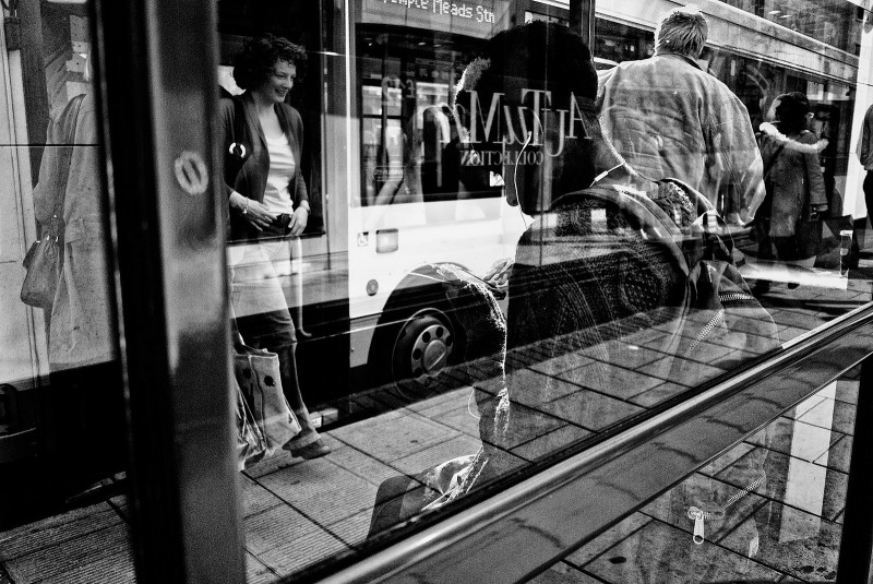 File: A bus stop seen through the rear of its glass shelter as passengers board a bus, disembark, or sit on the bench. The story of James Roberson's 21 mile commute on foot brought media attention to Detroit transit issues, but the story really highlights larger national issues. (Flickr / Brandon Chambers)