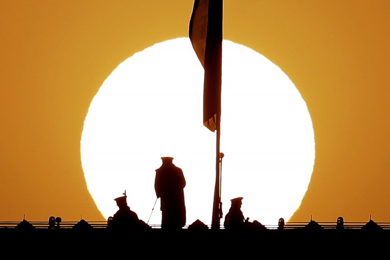 As the sun rises, Chinese paramilitary policemen watch over Tiananmen Square from a rooftop across from the Great Hall of the People ahead of the closing ceremony of the annual National People's Congress in the hall in Beijing on Sunday, March 15, 2015. Interest in China's Asian Infrastructure Investment Bank is growing, endangering America's formerly unbeatable control over global finance. (AP Photo/Andy Wong)