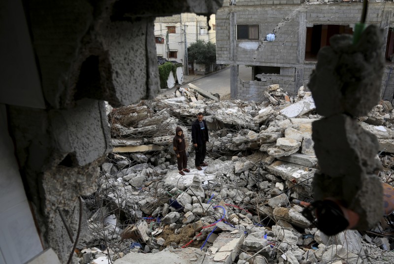 In this Wednesday, Nov. 26, 2014 photo, Mohammed Al-Bayoumi, 39, and his son Mahmoud pose for a portrait on the rubble of their family home in the Nusseirat refugee camp in the central Gaza Strip during a visit to the site with an Associated Press photographer. Obama and other allies continue to insist that repeated Israeli ceasefire violations and brutal aggression against Palestinian civilians are "self-defense," against all evidence to the contrary. (AP Photo/Adel Hana)