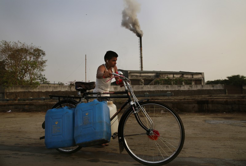 An Indian man pushes a cycle carrying water cans as smokes rises from a biomedical waste plant in Mumbai, India, Thursday, April 9, 2015. Air pollution kills millions of people every year, including more than 627,000 in India, according to the World Health Organization. The WHO puts 13 Indian cities in the world's 20 most polluted. (AP Photo/Rafiq Maqbool)