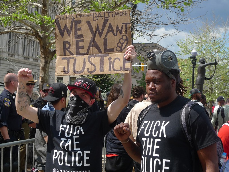 Two protesters attend a rally in Baltimore on May 2, 2015 wearing "Fuck the Police" T-shirts. One is holding a sign that reads, "Black Lives Matter Baltimore: We Want Real Justice." Based on past cases, many consider it unlikely that courts will convict the police that killed Freddie Gray. (Flickr / Susan Melkisethian)