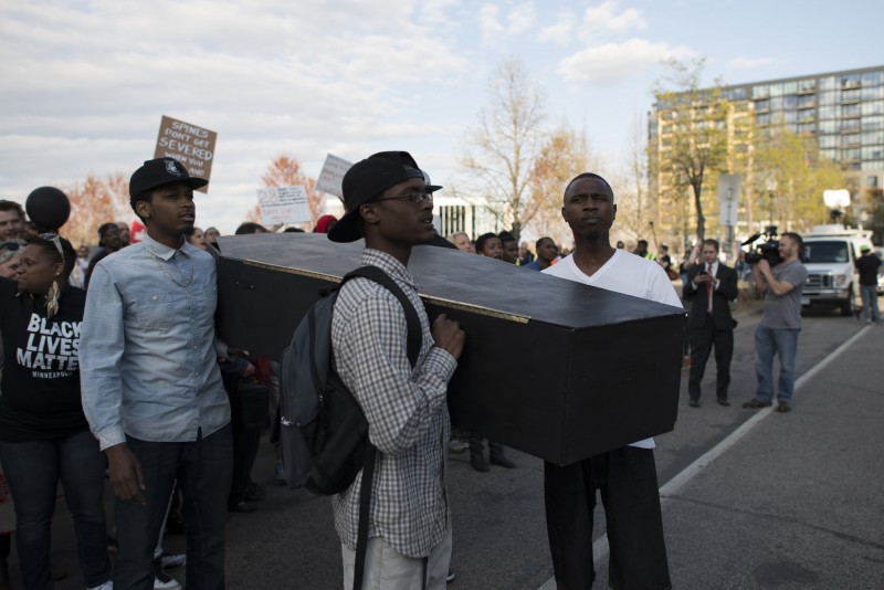 Three black men carry a mock coffin at a Black Lives Matter protest in Minneapolis on April 29, 2015. Systemic poverty and inequality are key issues in recent uprisings. (Flickr / Fibonacci Blue)