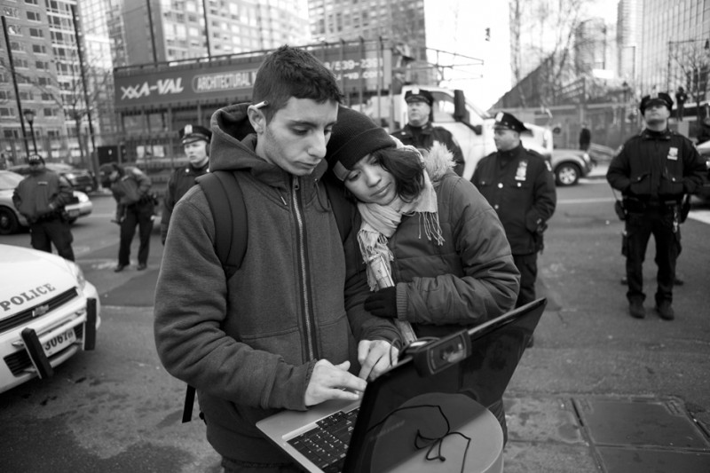A pair of citizen journalists stand close together as one types on a laptop in front of a row of police officers at an Occupy Wall Street protest on December 12, 2011. In revolutionary media, citizen journalists no longer try to remain neutral or removed from the action happening in the streets. (Flickr / Jessica Lehrman)