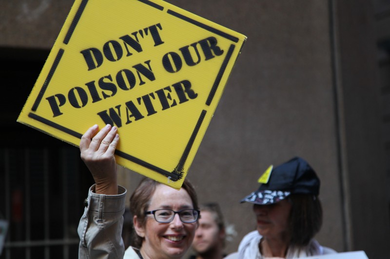 An activist holds a sign, designed to look like a roadside caution sign, that reads "DON'T POISON OUR WATER" at an anti-fracking protest in Sydney, Australia on October 23, 2014. New data shows that U.S. fracking is wasting millions of gallons water, even as drought worsens in many parts of the country. (Flickr / Kate Ausburn)