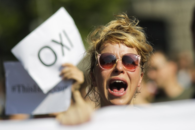 A women chants slogans and shows a poster reading 'NO' in Greek during a protest against the Greece acceptance of Germany's austerity demands prior to a special session of the parliament Bundestag on Greece for a new bailout in Berlin, Germany, Friday, July 17, 2015. (AP Photo/Markus Schreiber)