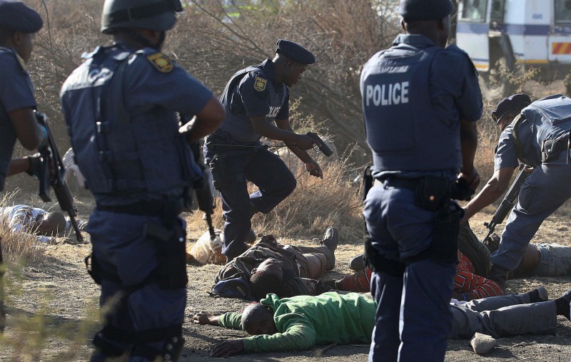 In this file photo taken Thursday, Aug. 16, 2012 police surround the bodies of striking miners after opening fire on a crowd at the Lonmin Platinum Mine near Rustenburg, South Africa. In a report read by president Jacob Zuma, Thursday, June 25, 2015 he said several steps should be taken to step up police work in situations such as those that occurred during the strike on the platinum belt in August 2012, which left at least 44 people dead. (AP Photo-File)