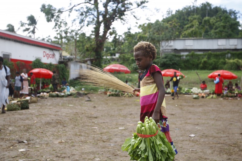 In this Saturday, May 30, 2015, photo, a girl carries goods at an outdoor market in Port Vila, Vanuatu. Many people in Vanuatu believe the nation is suffering the effects of climate change, including changes to crop seasons. (AP Photo/Nick Perry)