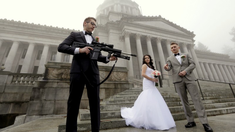 The best man in a wedding party, who all declined to be identified, holds an AR-10 rifle he was handed while the party was having their pre-wedding portraits taken on the steps of the capitol before a rally nearby by gun-rights advocates to protest a new expanded gun background check law in Washington state Saturday, Dec. 13, 2014, in Olympia, Wash. 