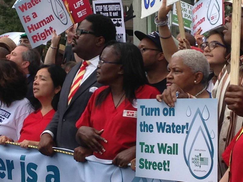 At a rally in opposition to water shut offs in Detroit, an activist holds a sign which reads, "Turn on he Water! Tax Wall Street!" (Flickr / Unitarian Universalist Service Committee)