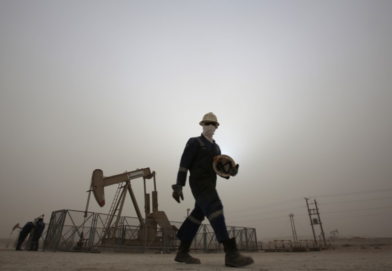 In this Thursday, Jan. 8, 2015 file photo, an oil worker walks by an oil pump during a sandstorm that blew in, in the desert oil fields of Sakhir, Bahrain. Across a Mideast fueled by oil production, low global prices have some countries running on empty and scrambling to cover shortfalls, even as more regional crude is on tap to enter the market.(AP Photo/Hasan Jamali, File)