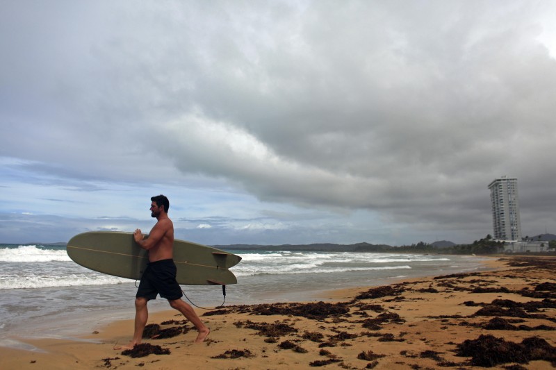 A surfer walks into the ocean as Tropical Storm Erika approaches the island in Luquillo, Puerto Rico, Thursday, Aug. 27, 2015. Tropical Storm Erika pummeled the eastern Caribbean island of Dominica, unleashing landslides and killing at least four people. The storm knocked out power and water supplies and had dumped 15 inches of rain on Dominica by early Thursday, according to the weather service in the nearby island of Antigua. (AP Photo/Ricardo Arduengo)
