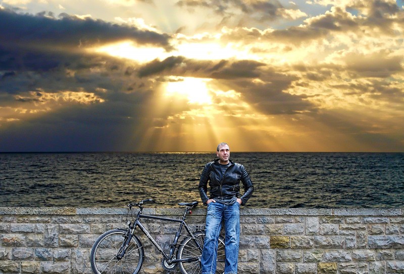 A man leans with his bicycle against a stone wall by the edge of the Atlantic Ocean at sunset. (Flickr / driver Photographer)