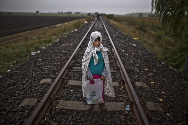 In this photo taken on Friday, Sept. 11, 2015, Syrian refugee Yasmeen Alhawal, 5, who came with her father Khalil from Aleppo, Syria, poses for a picture holding a bag of her belongings as they make their way through the railway at the Serbian-Hungarian border near Roszke, southern Hungary. We just want to go to a country that treat us like humans. Our homes were destroyed, daily terrified not only from Bashar Assad but also from Islamic State, IS," said Yasmeen's father, Khalid Alhawal. (AP Photo/Muhammed Muheisen)