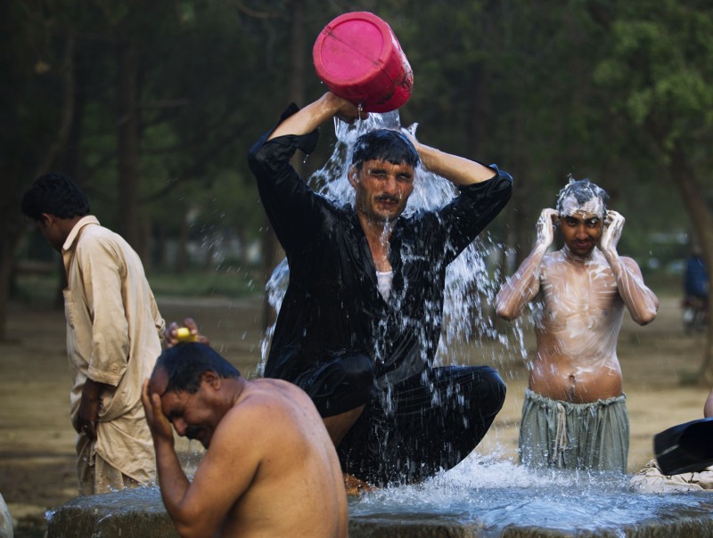 In this June 3, 2013 file photo, Pakistani laborers bathe at a leaked water hydrant at the end of a day on the outskirts of Islamabad. With each degree, unrestrained global warming will singe the overall economies of three quarters of the nations in the world and widen the north-south gap between rich and poor countries, a new economic and science study found. Compared to what it would be without more global warming, the average income globally will shrivel 23 percent at the end of the century if heat-trapping carbon dioxide pollution continues to grow at current trajectories, according to a study published Wednesday in the scientific journal Nature. (AP Photo/B.K. Bangash, File)