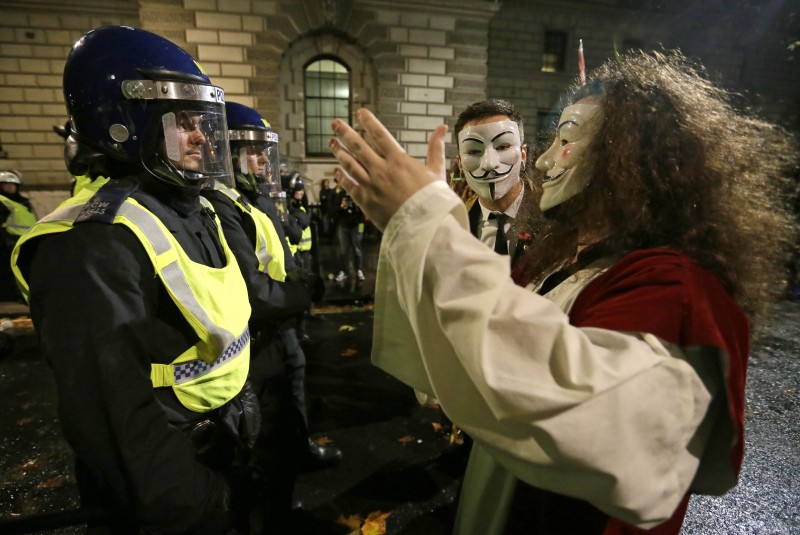 A masked demonstrator reaches out to greet a police officer blocking his way during the Million Mask protest march in London on Thursday Nov. 5, 2015. Thousands of people dressed in Guy Fawkes masks are being met by significant policing operation, including thousands of extra officers to tackle expected unrest in this annual march that coincides with the Nov. 5 Bonfire Night celebration. (AP Photo/Tim Ireland)
