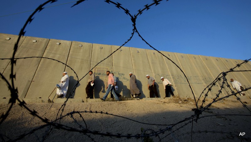 Palestinian men walk past a section of Israel's apartheid wall on their way to pray at the Al-Aqsa Mosque in Jerusalem, on the fourth Friday of the Muslim holy month of Ramadan, at the Qalandia checkpoint between the West Bank city of Ramallah and Jerusalem, Friday, July 10, 2015. 