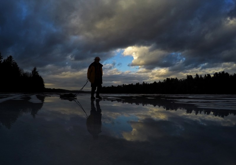 Andrew Cash heads for home after an unsuccessful afternoon of ice fishing for trout on Sabbathday Lake, Thursday, Feb. 25, 2016, in New Gloucester, Maine. Wednesday's rain storm and Thursday's temperatures in the mid-50s left a reflective layer of water on top of the ice. (AP Photo/Robert F. Bukaty)