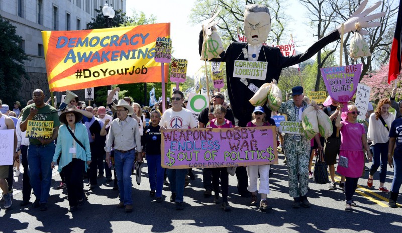 Thousands gathered around the U.S. Capitol on April 17, 2016 to oppose corruption in politics. In this photo, activists carry a #DemocracyAwakening banner, a corporate lobbyist puppet, and a CODEPINK Anti-war banner. (Flickr / Stephen Melkisethian)