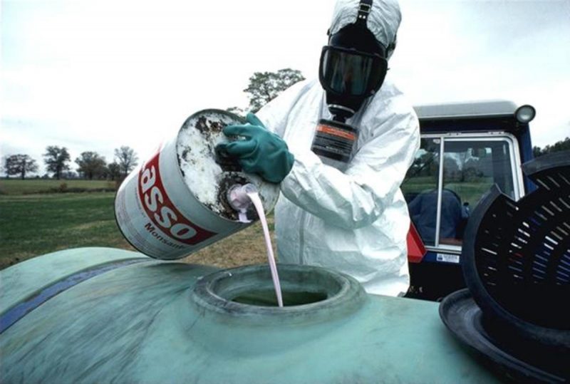 A man in a hazardous material suit pours herbicide for use on an industrial farm. (AP)