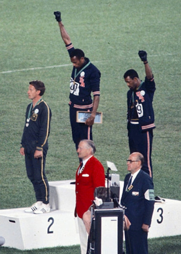 Gold medallist Tommie Smith (center) and bronze medalist John Carlos (right) showing the raised fist on the podium after the 200 m race at the 1968 Summer Olympics; both wear Olympic Project for Human Rights badges. Peter Norman (silver medalist, left) from Australia also wears an OPHR badge in solidarity to Smith and Carlos. (Wikimedia Commons / Mondadori Publishers / Angelo Cozzi)