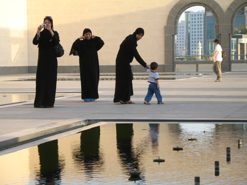 Three women in abaya and a young child stand by a reflecting pool at the Museum of Islamic Art, Doha Qatar. October 9, 2010. (Flickr / Kevin Burden)