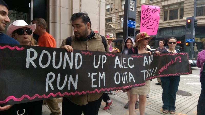 At a July 31, 2014 CODEPINK Rally outside Neiman Marcus in Dallas, Texas, activists hold a banner reading “Round Up ALEC and Run ‘Em Outa Town.” (Kit O’Connell)