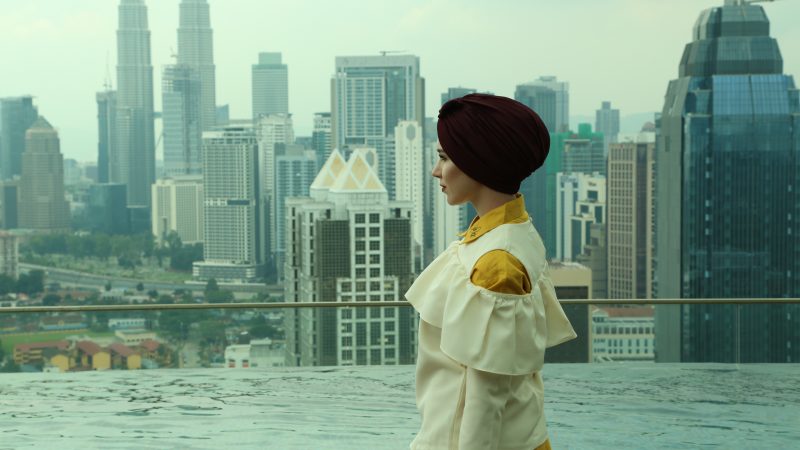 A woman in an outfit created by the "modest fashion" designer Nabiilabee stands in front of an urban city skyline. (Photo © Nabiilabee, used with permission.)