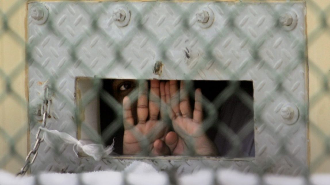 In this Dec. 4, 2006 file photo, reviewed by a U.S. Department of Defense official, a detainee shields his face as he peers out through the so-called "bean hole" which is used to pass food and other items into detainee cells, in Camp Delta detention facility at the Guantanamo Bay U.S. Naval Base in Cuba. (AP Photo/Brennan Linsley, File)