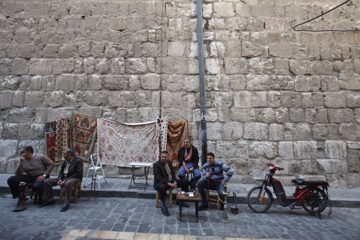 Tapestries are displayed as men sit outside the Omayyid mosque in old Damascus, Syria, Thursday, March 22, 2012. Mounting international condemnation of Bashar Assad's regime and high-level diplomacy have failed to ease the year-old Syria conflict, which the U.N. says has killed more than 8,000 people. (AP Photo/Muzaffar Salman)