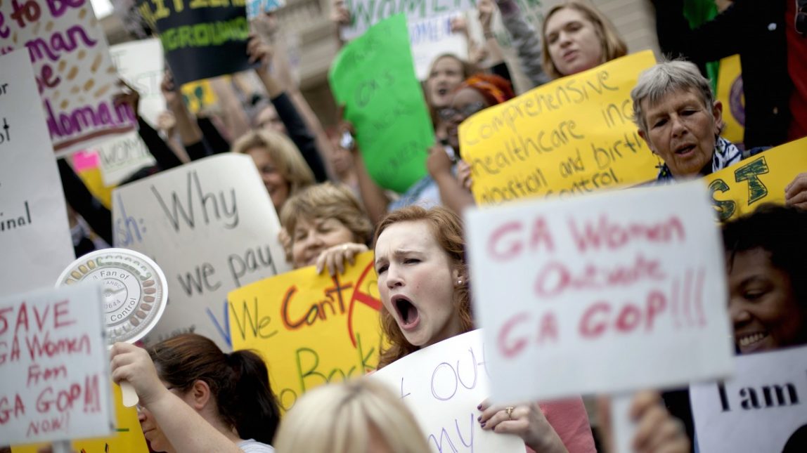Aly Bancroft, center, of Atlanta, joins hundreds of people around the Georgia Capitol protesting against two pieces of legislation they say are unfair to women, Monday, March 12, 2012, in Atlanta. (AP Photo/David Goldman)