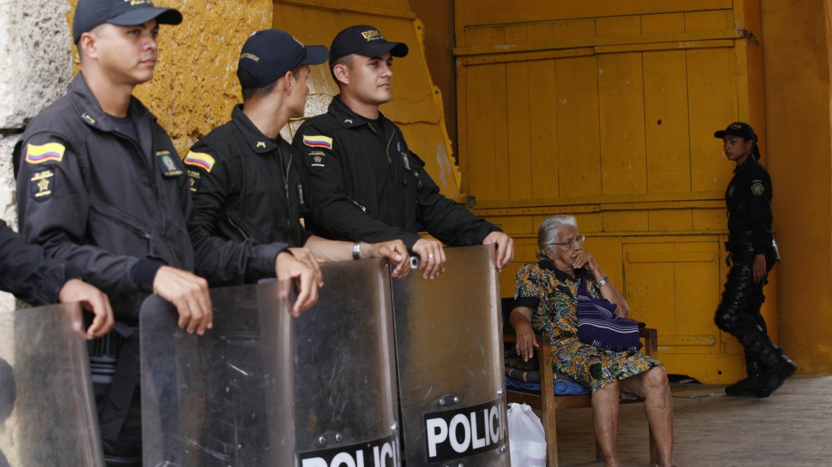 An elderly woman sits as police officers stand guard in Cartagena, Colombia, Thursday, April 12, 2012. Leaders of the western hemisphere will attend the 6th Summit of the Americas in Cartagena on April 14 and April 15. (AP Photo/Dolores Ochoa)