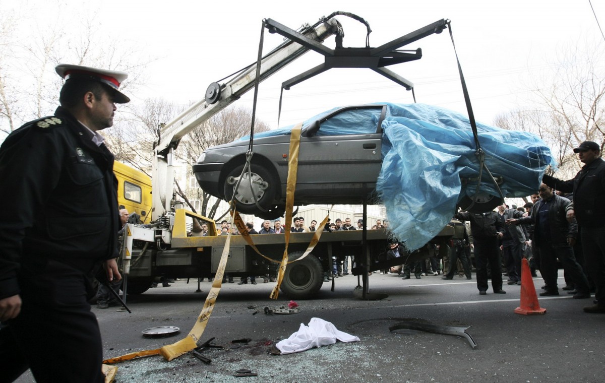 In this photo provided by the semi-official Fars News Agency, people gather around a car as it is removed by a mobile crane in Tehran, Iran, Wednesday, Jan. 11, 2012. Two assailants on a motorcycle attached magnetic bombs to the car of an Iranian university professor working at a key nuclear facility, killing him and wounding two people on Wednesday, a semiofficial news agency reported. (AP Photo/Fars News Agency, Meghdad Madadi)