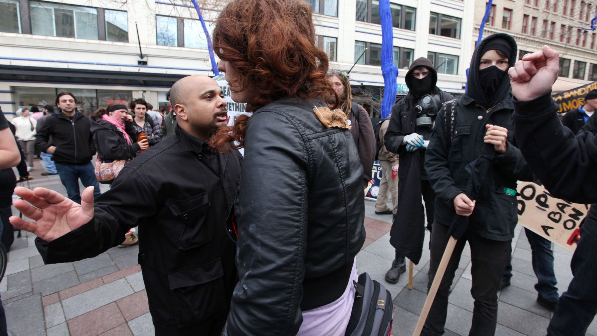 Black-clad protesters, some holding sticks or wearing masks and hoods, argue with a man at left who confronted them about violence nearby earlier in the day Tuesday, May 1, 2012, in downtown Seattle. (AP Photo/Elaine Thompson)