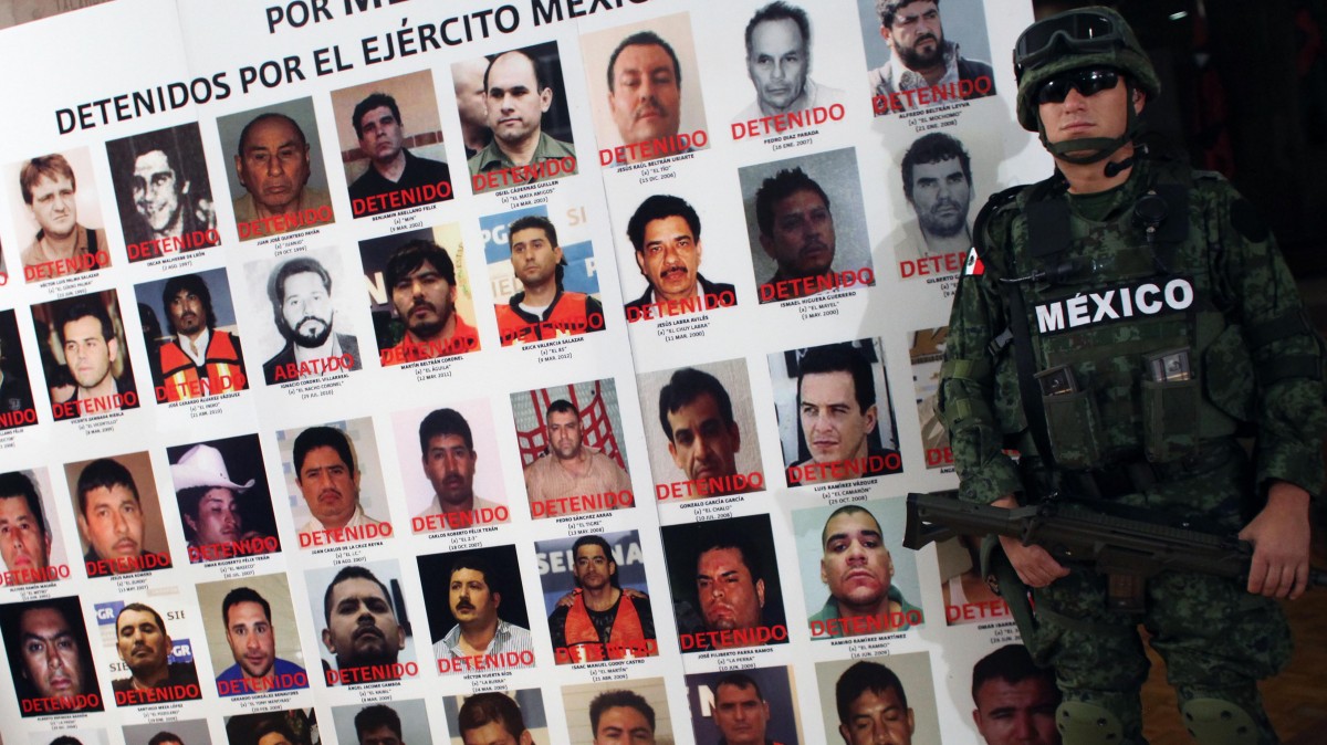 An army soldier stands next to a banner displaying mug shots of persons detained or killed by the Mexican Army Monday, May 21, 2012. (AP Photo/Alexandre Meneghini)