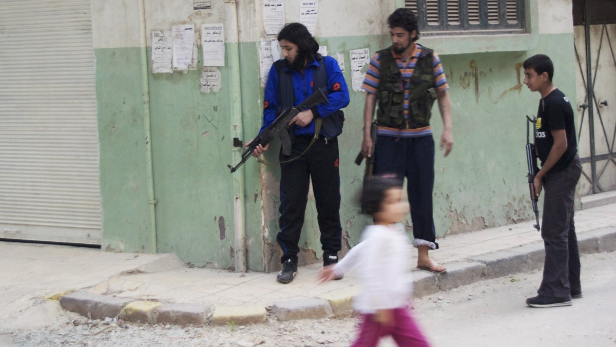 In this Monday, May 14, 2012 photo, a girl walks past Syrian rebels at Khaldiyeh neighborhood in Homs province, central Syria. The violence around the country is eroding an internationally brokered peace plan that many U.N. observers see as the last hope to calm the 14-month-old crisis. (AP Photo/Fadi Zaidan)