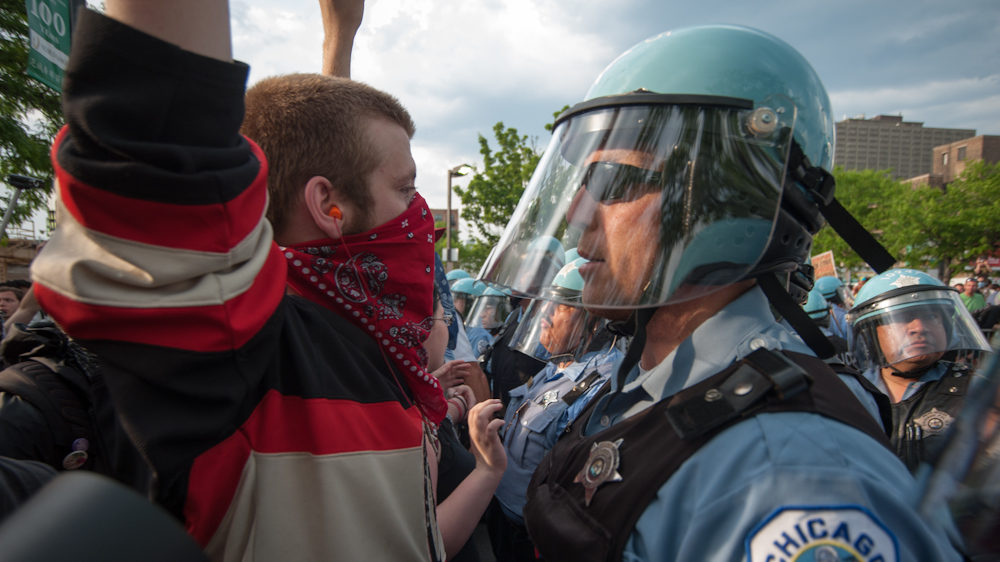 Protesters and police face off during demonstrations against NATO. Protesters wore earplugs to counter the effects of LRADs that were brought into the streets by the police force. (Photo Norbert Schiller/Mint Press)