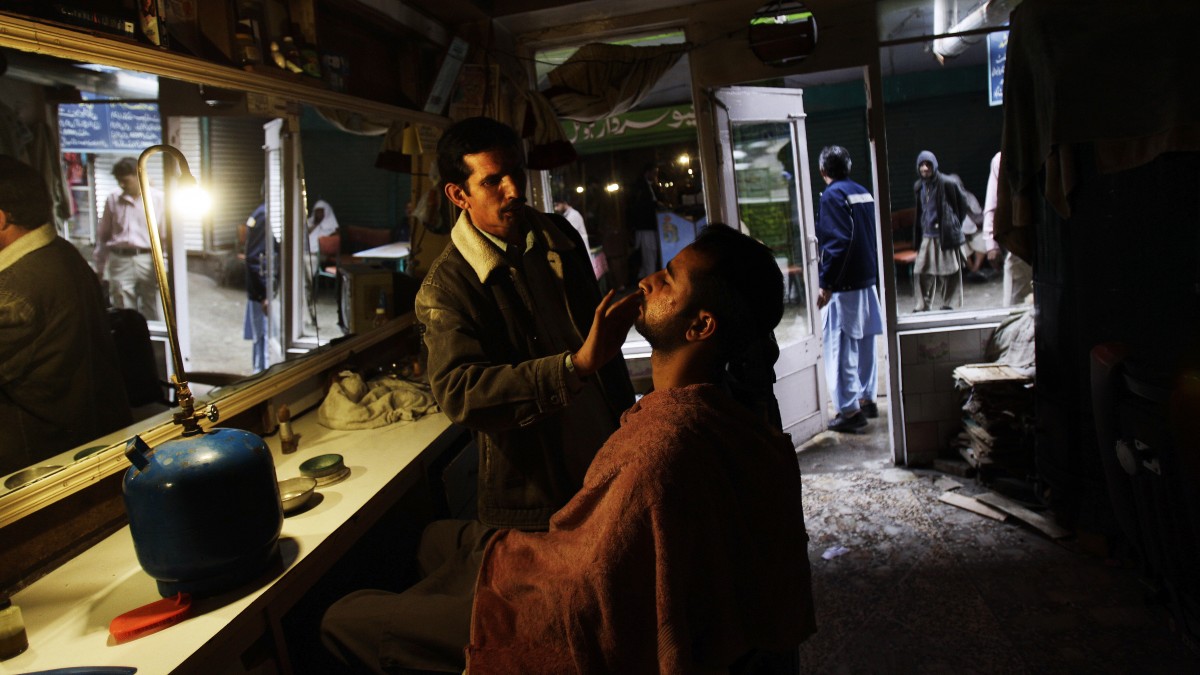 In a Sunday, April 29, 2012, photo, Pakistani barber Mohammed Arif, 35, lights his shop with a lamp due to a power cut, while shaving a customer, in Abbottabad, Pakistan. David Walters saw a business opportunity where few other foreign investors would think of treading: Pakistan's power sector. He saw profit in importing power stations, linking them to the national grid and selling the electricity to the energy-starved country. (AP Photo/Muhammed Muheisen)