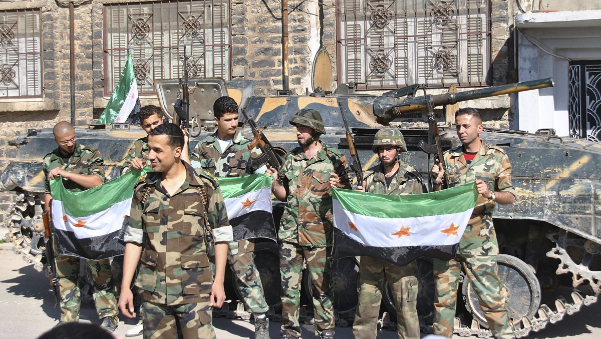 Syrian army soldiers, hold the Syrian revolution flags as they stand in front their armored personnel carrier shortly after they defected and join the rebels, at Khaldiyeh neighborhood, in Homs province, central Syria, Saturday May 12, 2012. Syria's uprising started in March 2011 with mostly peaceful protests inspired by successful revolts elsewhere calling for political reform. The Syrian government responded with a brutal crackdown, prompting many in the opposition to take up arms to defend themselves and attack government troops. (AP Photo/Fadi Zaidan)