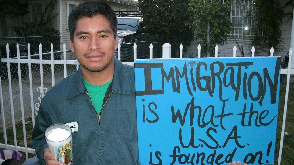A man stands holding a sign promoting immigration. (Photo by mpeake from Flikr)