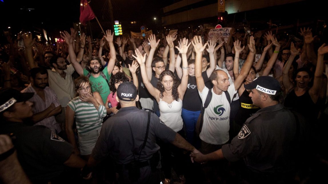 Israeli activists raise their hands during a social protest in Tel Aviv, Israel early Sunday, June 24, 2012. Israeli police say 85 protesters were arrested on Saturday after clashing with officers and vandalizing banks in Tel Aviv. (AP Photo/Dan Balilty)