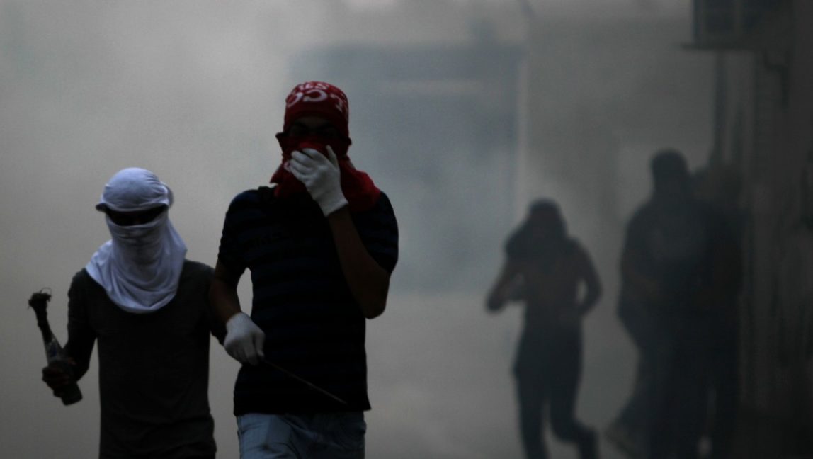 Bahraini anti-government protesters carrying a prepared Molotov cocktail and a steel bar run through tear gas fired by riot police during clashes Thursday, March 15, 2012, in the eastern town of Sitra, Bahrain. The clashes erupted during protests marking the one-year anniversary of a major crackdown on Sitra, an area that has seen some of the strongest anti-government unrest. (AP Photo/Hasan Jamali)
