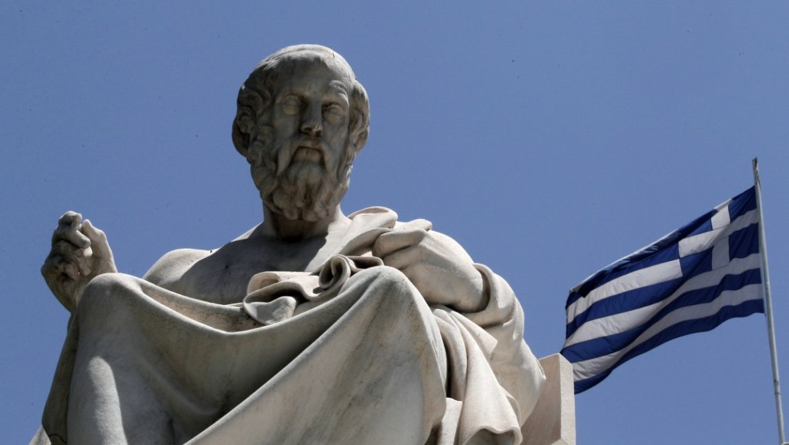The marble statues of ancient Greek philosophers Plato, stand in front of the Athens Academy, as the Greek flag flies in Athens on Tuesday June 5, 2012. (AP Photo/Dimitri Messinis)