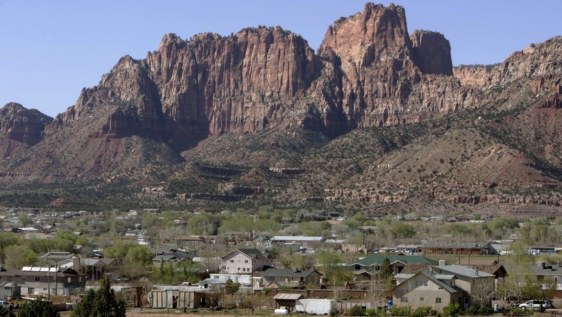 Hildale, Utah sits at the base of red rock cliff mountains with its sister city, Colorado City, Ariz. in the foreground in this Thursday, April 20, 2006 file photo. An attorney for local law enforcement in the two polygamous towns, where most residents are members of the Fundamentalist Church of Jesus Christ of Latter Day Saints run by the groupâs jailed leader Warren Jeffs, says the U.S. Justice Department plans to sue both communities, claiming religious discrimination. (AP Photo/Douglas C. Pizac)
