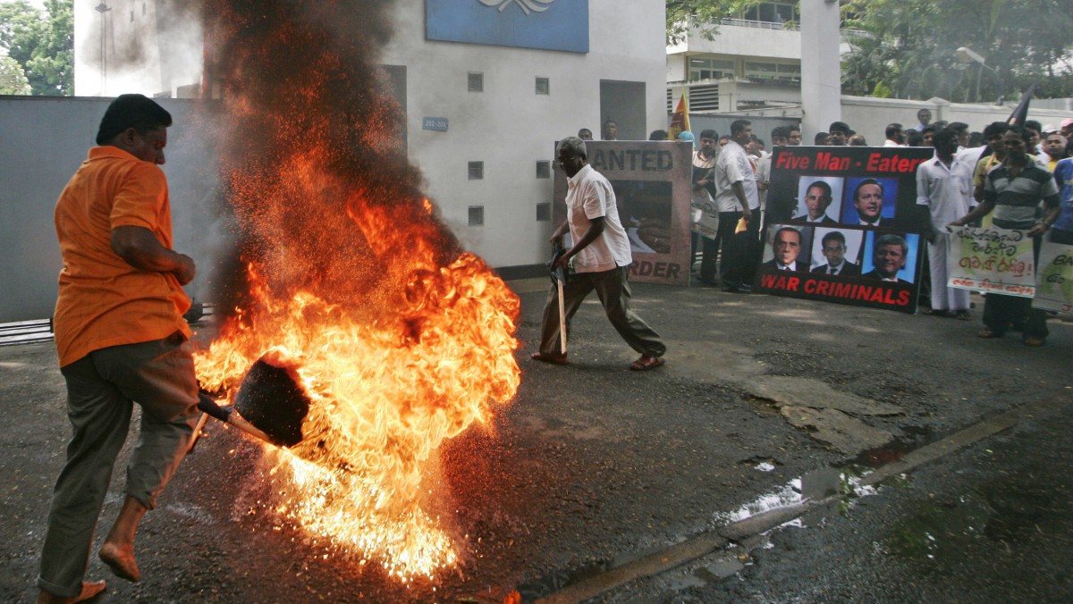 Members of the National Freedom Front hold placards as they burn tyres outside the UN office during a protest against the military attack on Libya by International coalition forces. (AP Photo/Chamila Karunarathne)