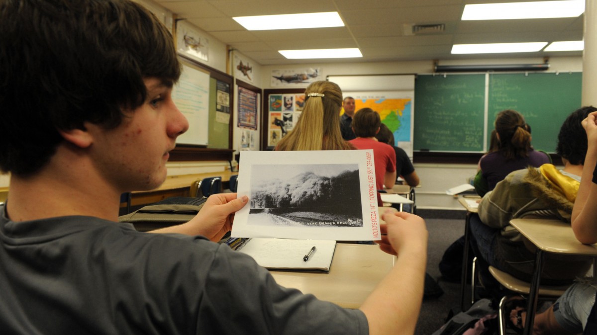 Pocatello High School sophomore Doug Walker shows a fellow student a class handout during Jeb Harrison's economics class in Pocatello, Idaho, of a print of a duststorm during the Great Depression. Across the bottom of the handout is an advertisement for a Molto Caldo pizza. The pizzeria donated the paper for use in Harrison's class. (AP Photo/Bill Schaefer)