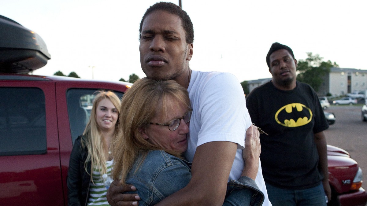 Judy Goos, center left, hugs her daughter's friend, Isaiah Bow, 20, while eyewitnesses Emma Goos, 19, left, and Terrell Wallin, 20, right, gather outside Gateway High School where witnesses were brought for questioning Friday, July 20, 2012, in Aurora, Colo. A gunman wearing a gas mask set off an unknown gas and fired into a crowded movie theater at a midnight opening of the Batman movie "The Dark Knight Rises," killing at least 12 people and injuring at least 50 others, authorities said. (AP Photo/Barry Gutierrez)