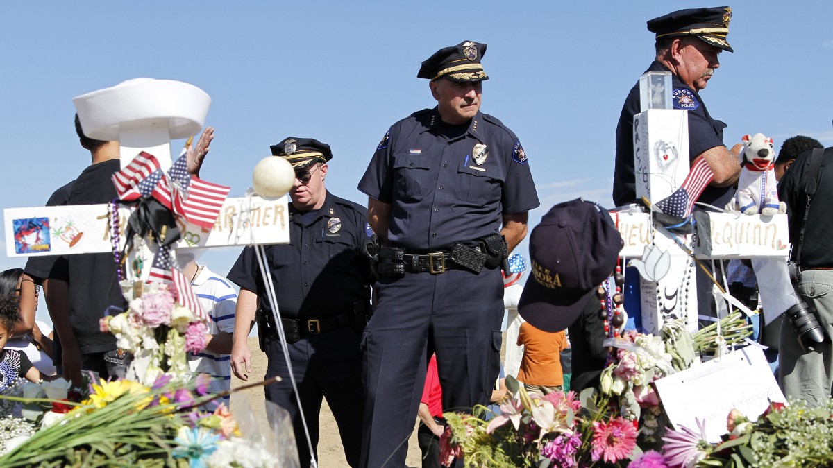 Aurora Police Chief Daniel Oates, center, looks at the memorial across from the movie theater, Wednesday, July 25, 2012 in Aurora, Colo. Twelve people were killed and more than 50 wounded in a shooting attack at the packed theater during a showing of the Batman movie, "The Dark Knight Rises." (AP Photo/Alex Brandon)